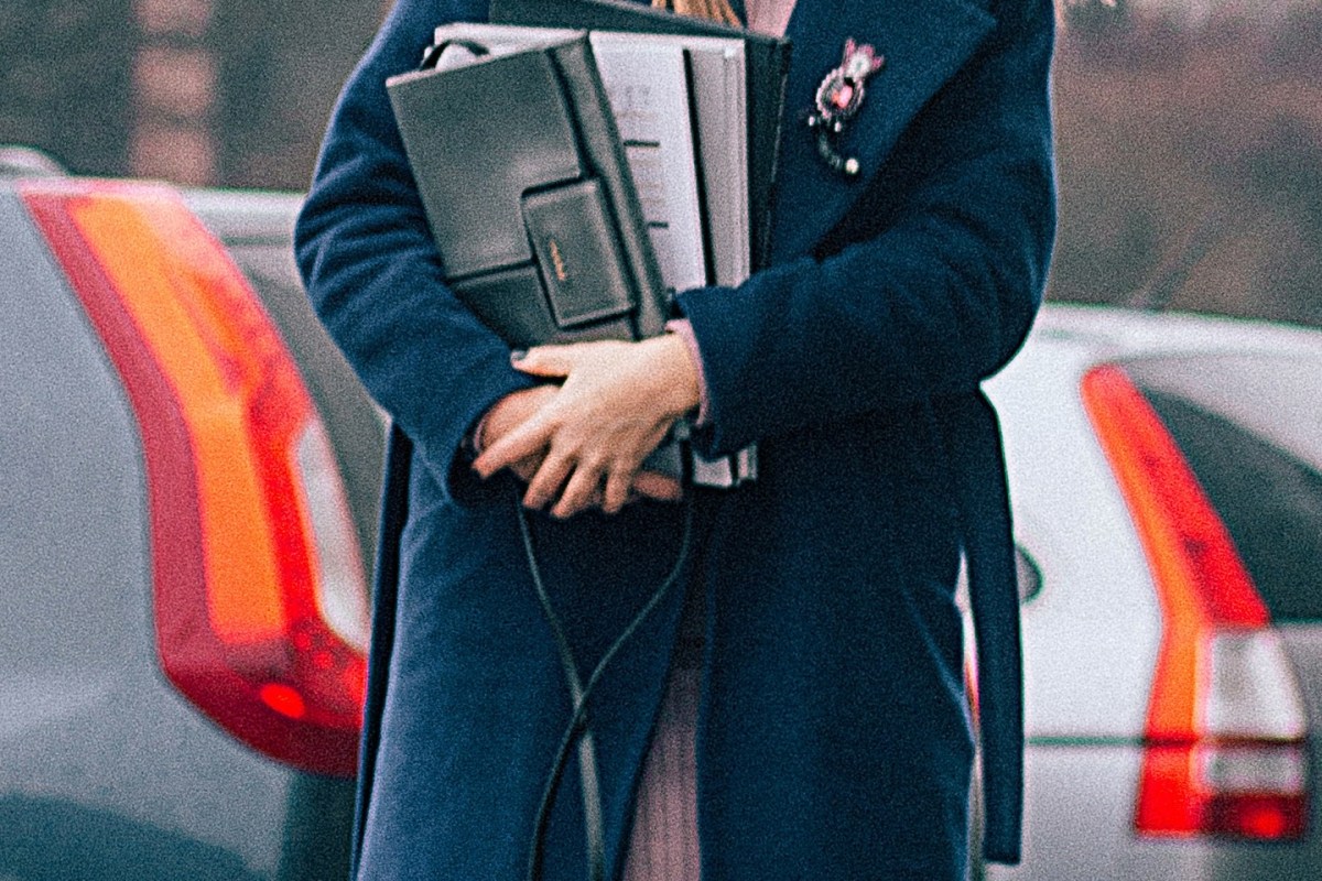 closeup of a female student carrying books while standing on a sidewalk with parked cars