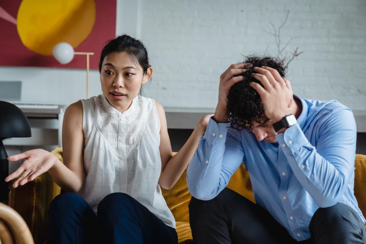 A couple sitting on a yellow couch while arguing.