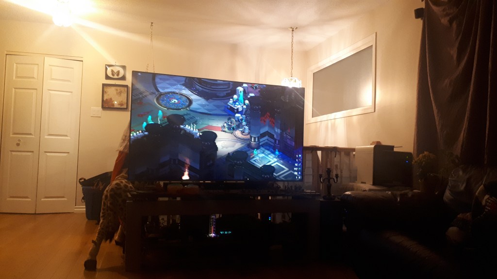 Living room with TV screen displaying a game named Hades, image is a castle with monsters the player is trying to defeat. 