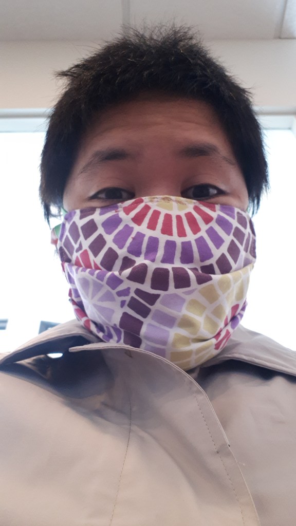 Selfie of woman wearing a fabric face mask, the horizontal accordion style. 