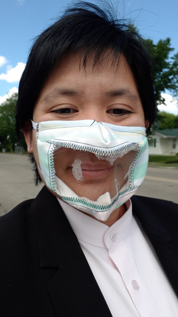 Selfie of woman wearing a fabric face mask with a plastic transparent window. 