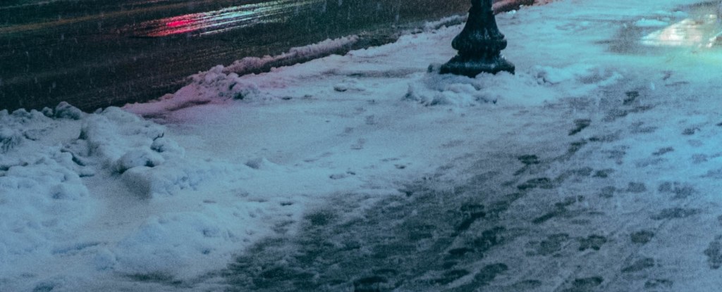 A sidewalk in the spring time, with snow and slush piled up. 